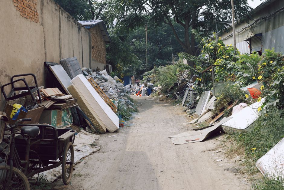 A large collection of discarded electronic devices, primarily comprising old computer monitors and CRT screens, stacked and piled together in an indoor environment. The monitors vary in size and desig